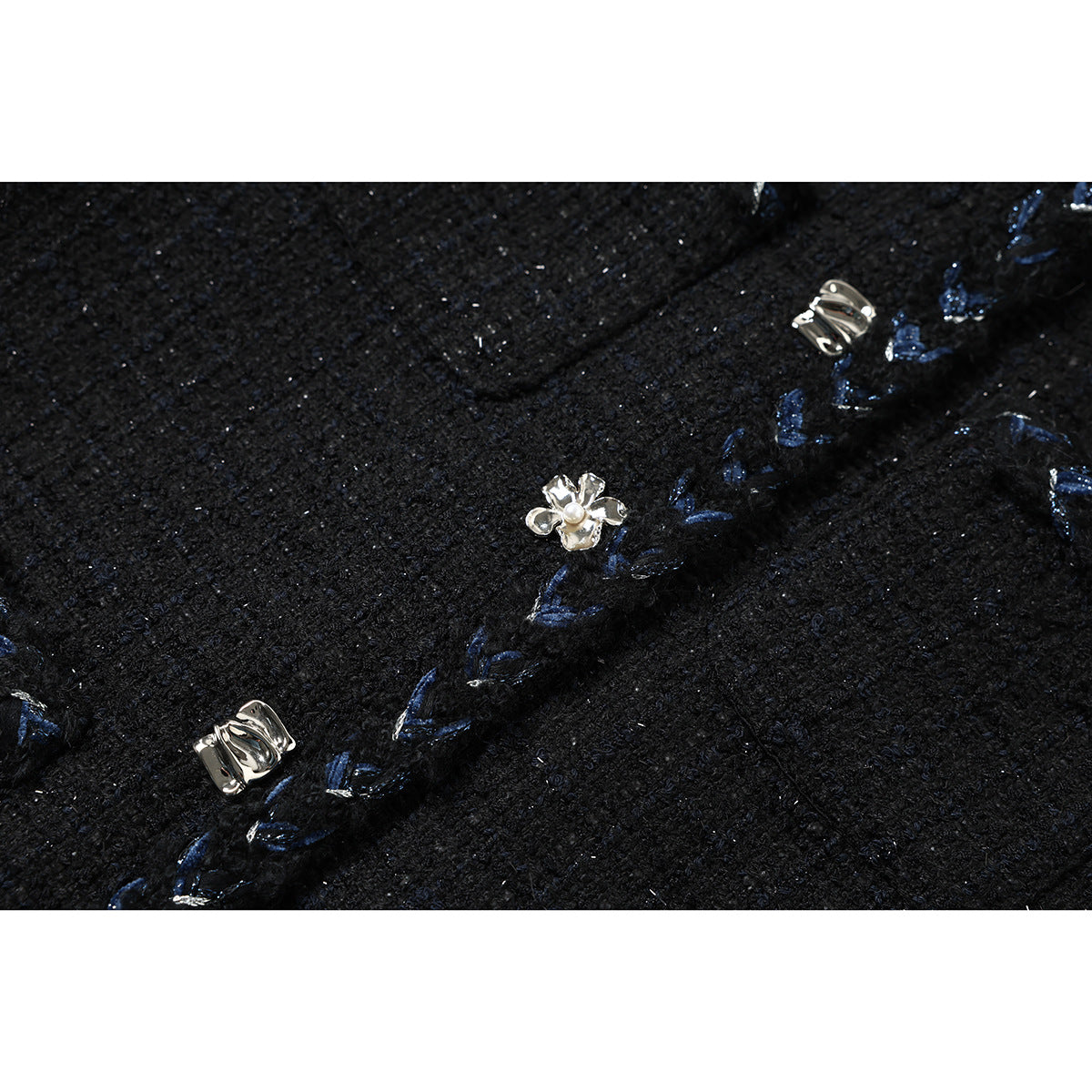 Close-up of black textured jacket fabric, blue embroidered edging, and decorative silver-tone fasteners with a flower
