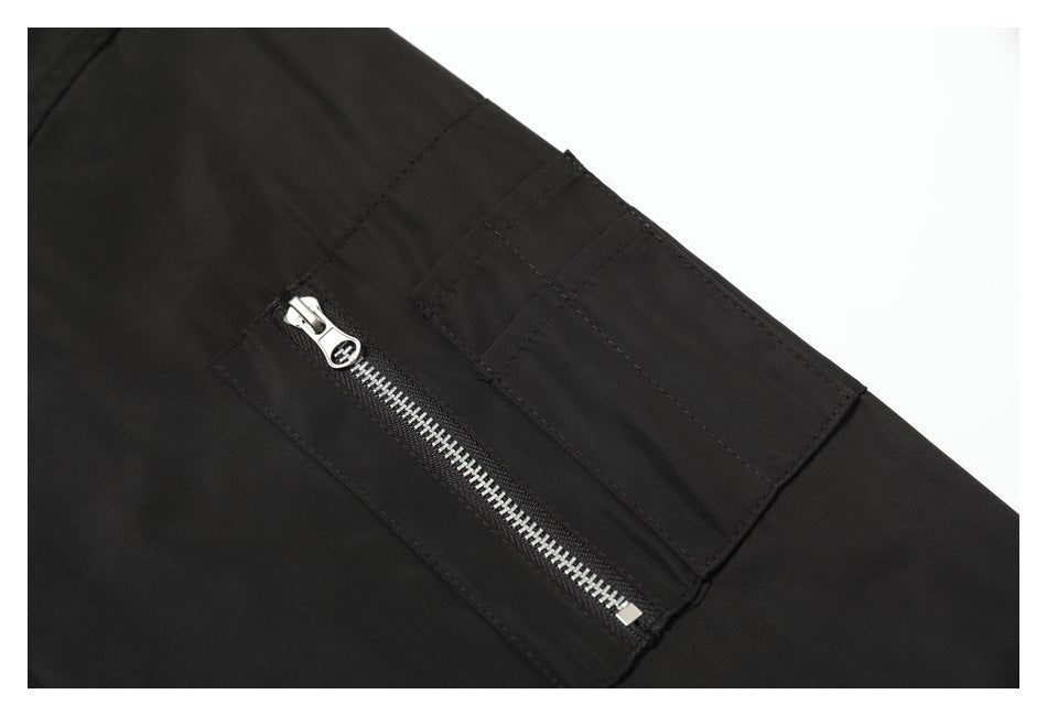 Close-up of a black jacket sleeve with a silver zipper pocket and a rectangular stitched pocket panel.