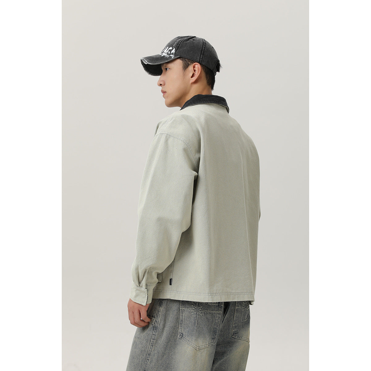 Rear three-quarter view of a model wearing a pale sage jacket with a black collar and a plain back.