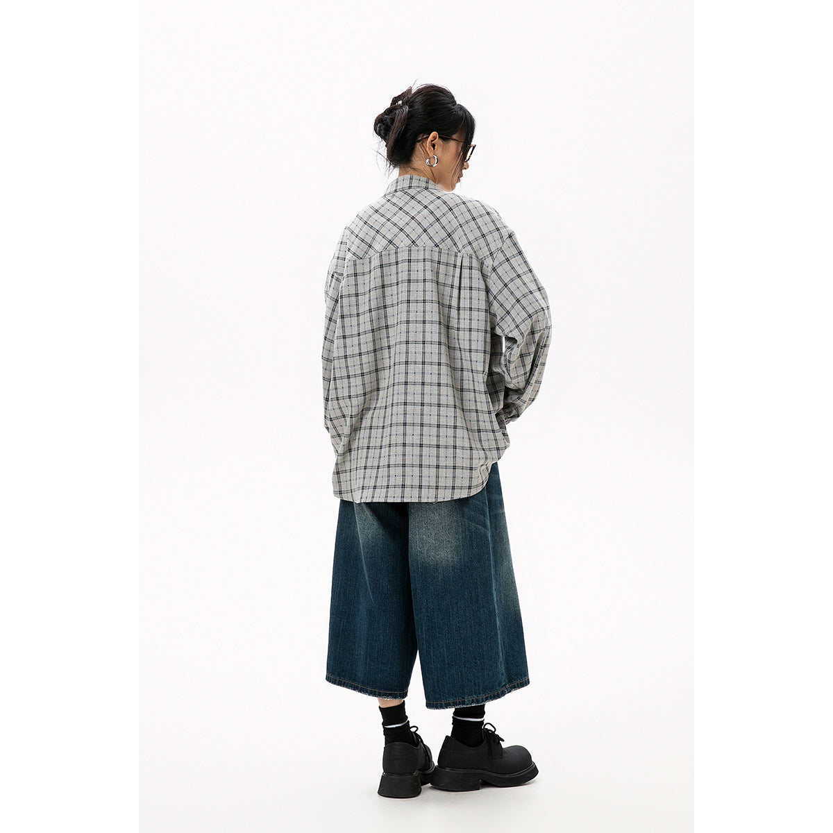 Rear view of a model wearing a gray plaid blouse with a gathered back yoke and dark wide-leg cropped jeans.