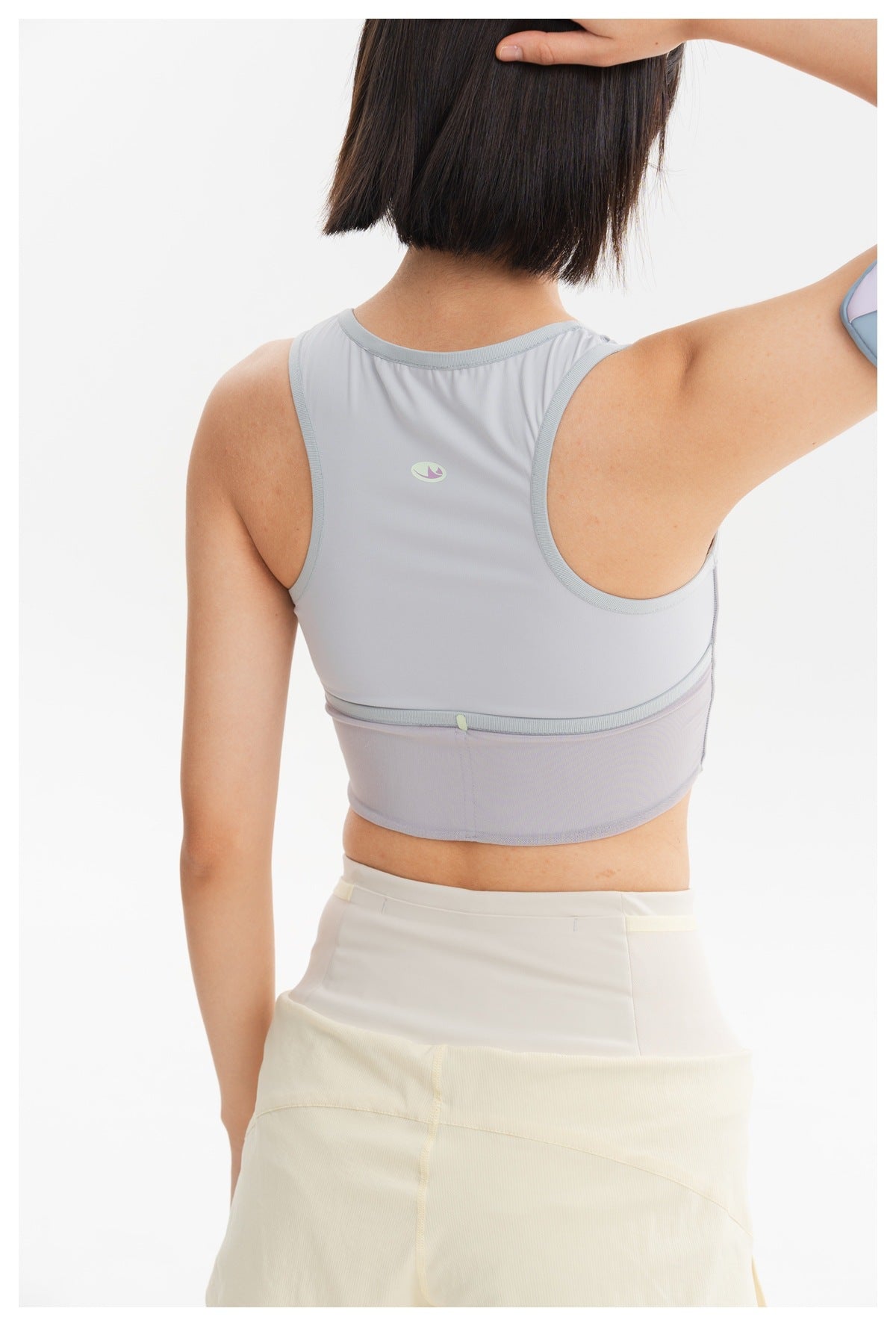 Rear view of a model wearing a light gray racerback crop top and pale yellow shorts.