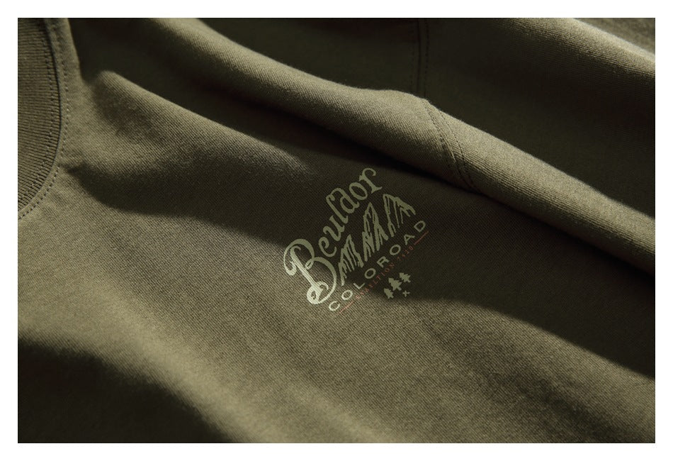 Close-up of a small cream Colorado-themed graphic printed on olive green T-shirt fabric.