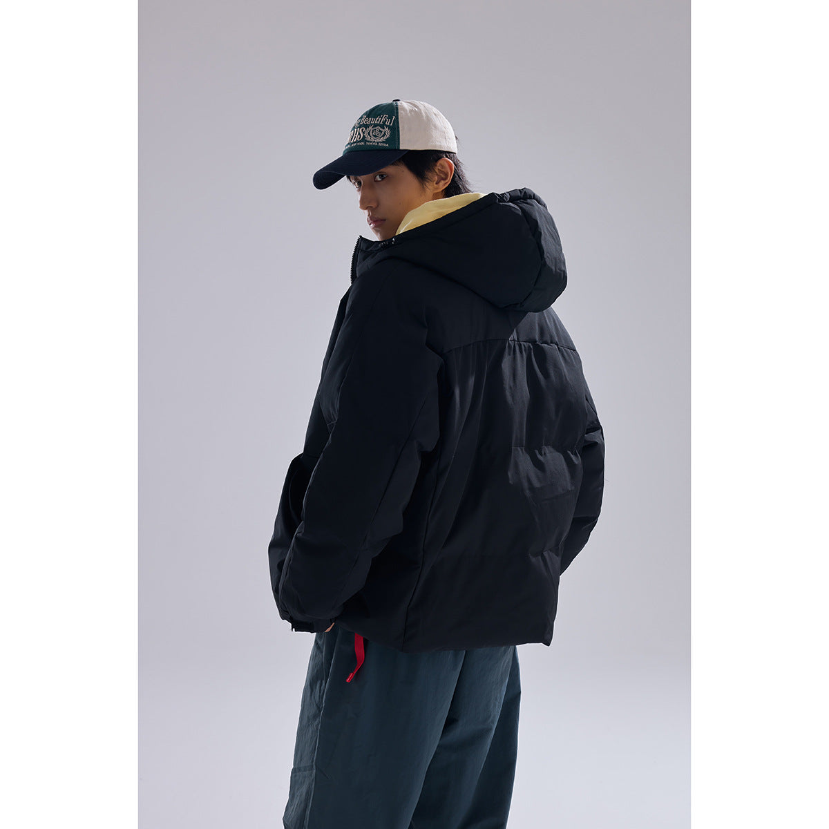 Model wearing a black hooded puffer jacket and dark pants, turned to show the jacket's back.