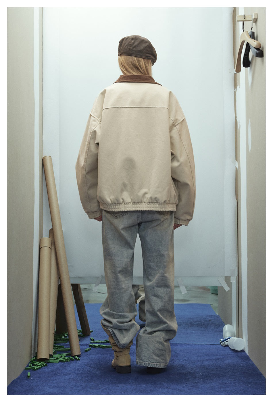 Rear view of a model wearing a loose cream jacket with a brown collar and gathered hem.