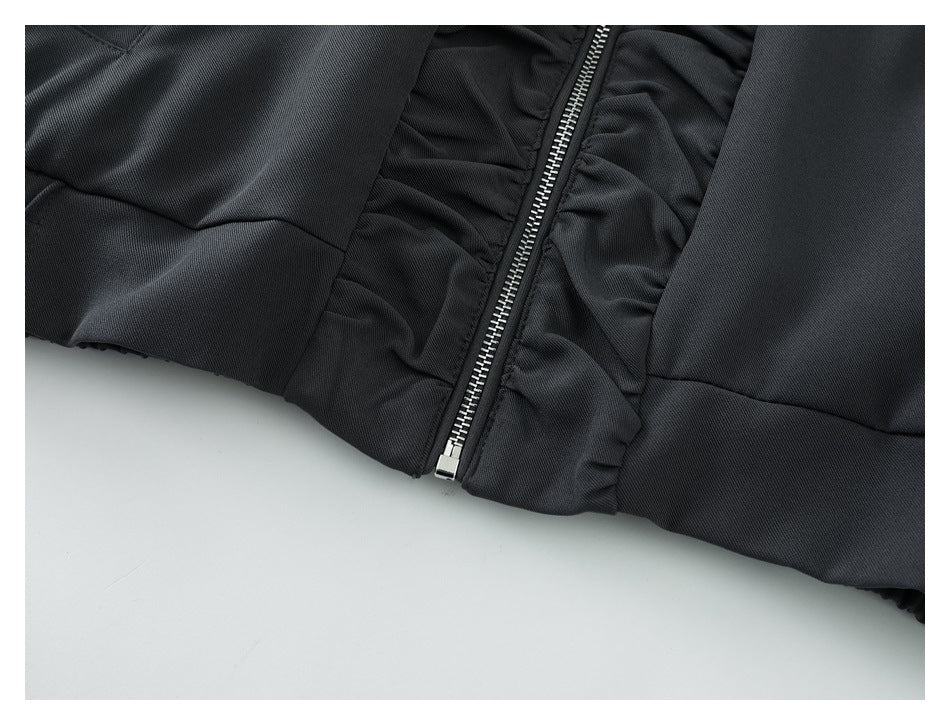 Close-up of a black garment showing a silver front zipper and gathered fabric panels.