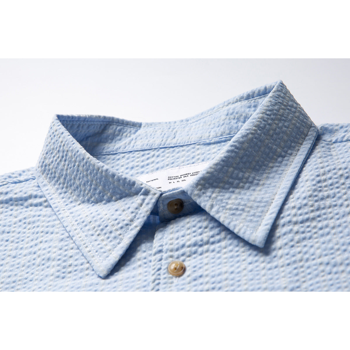 Close-up of a light blue textured shirt collar and buttons, with a small interior label visible.