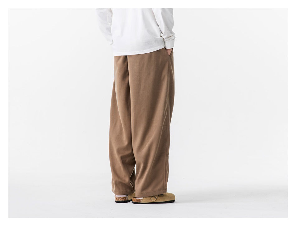 Rear view of a person wearing loose taupe-brown trousers with a white long-sleeve shirt.