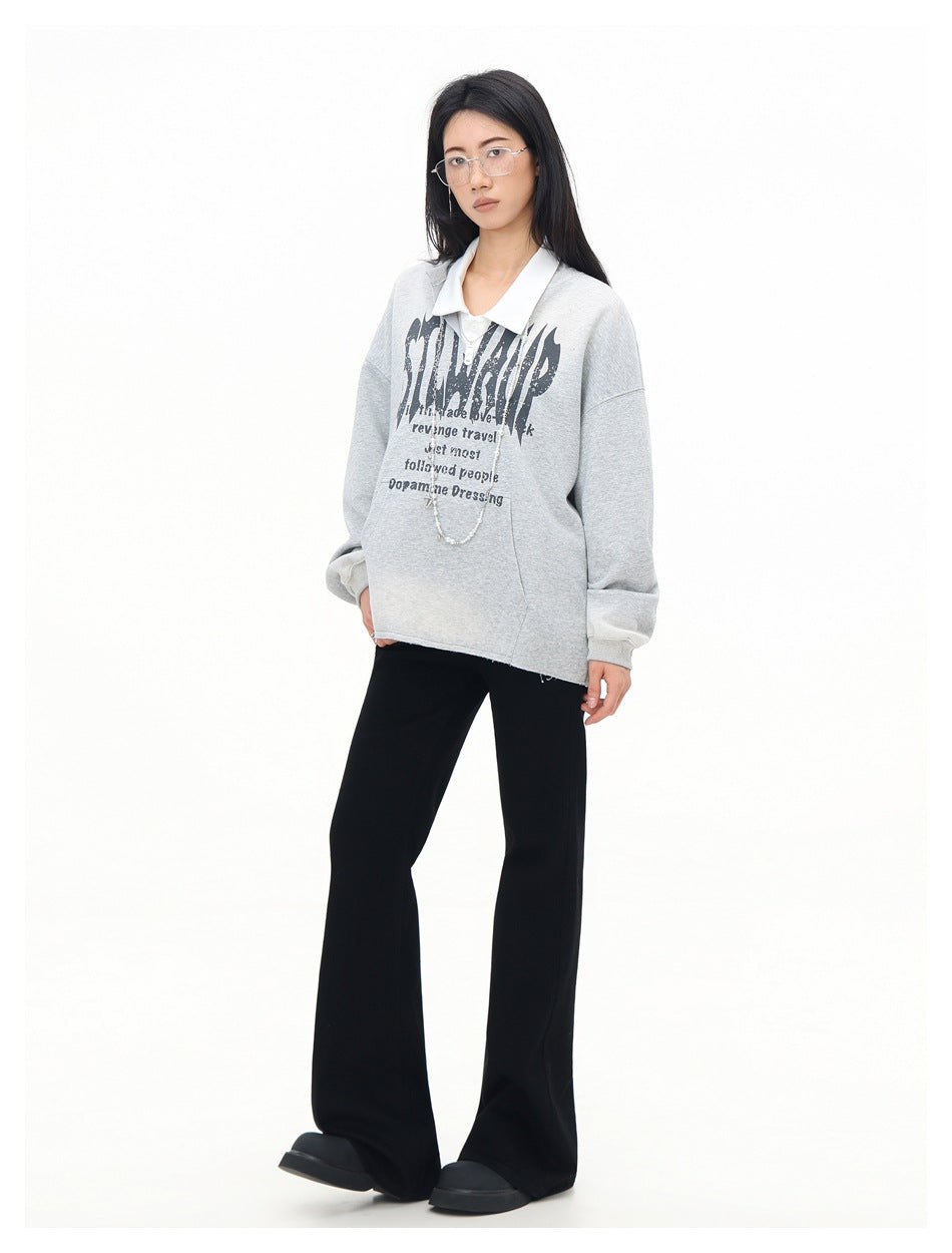 Three-quarter view of a model in a light gray graphic pullover over a white collar and black flared pants.