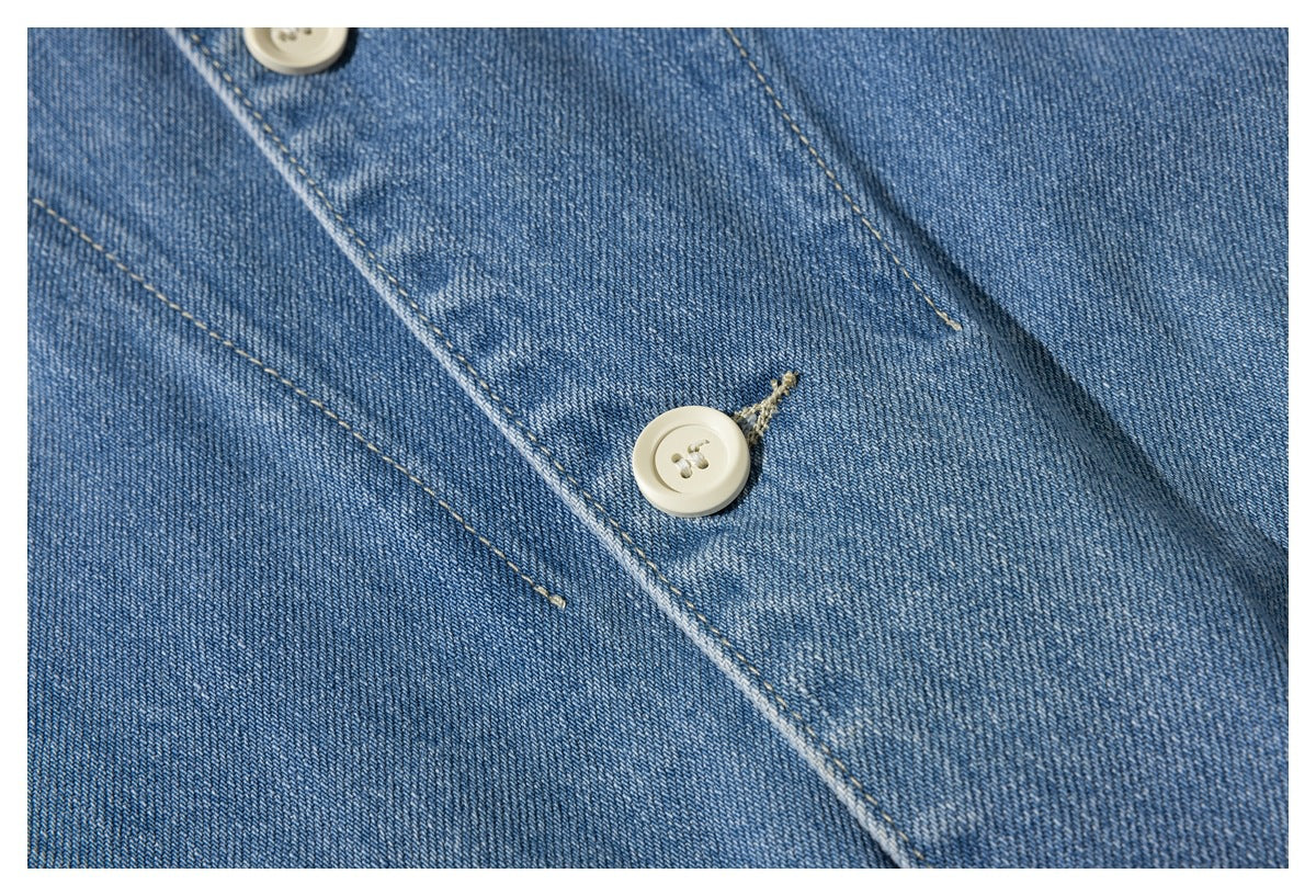 Close-up of a cream button and tan stitching on the blue denim jacket's front placket.