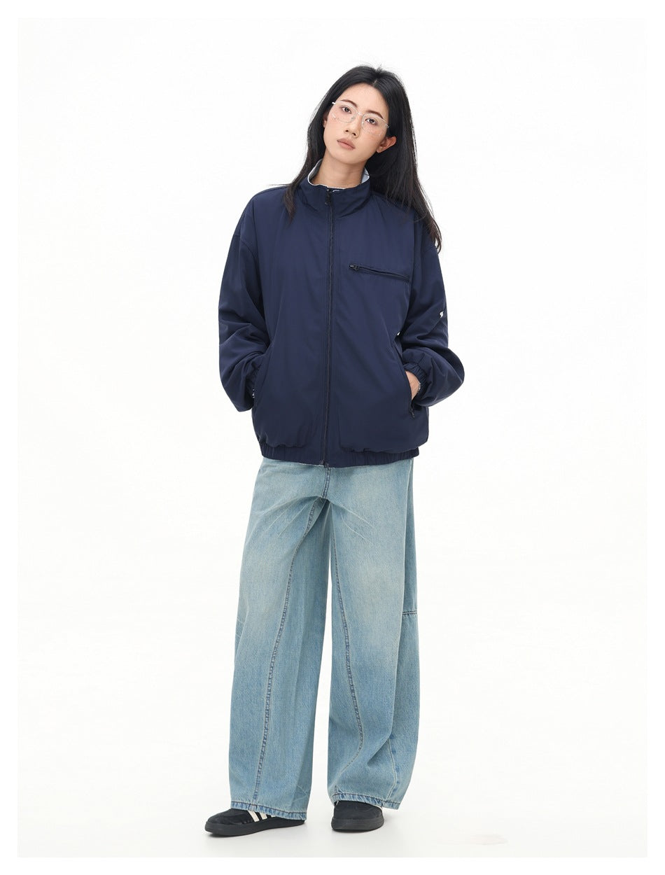 Model wearing a navy zip-front jacket with a stand collar and chest zip pocket, paired with light blue wide-leg jeans.