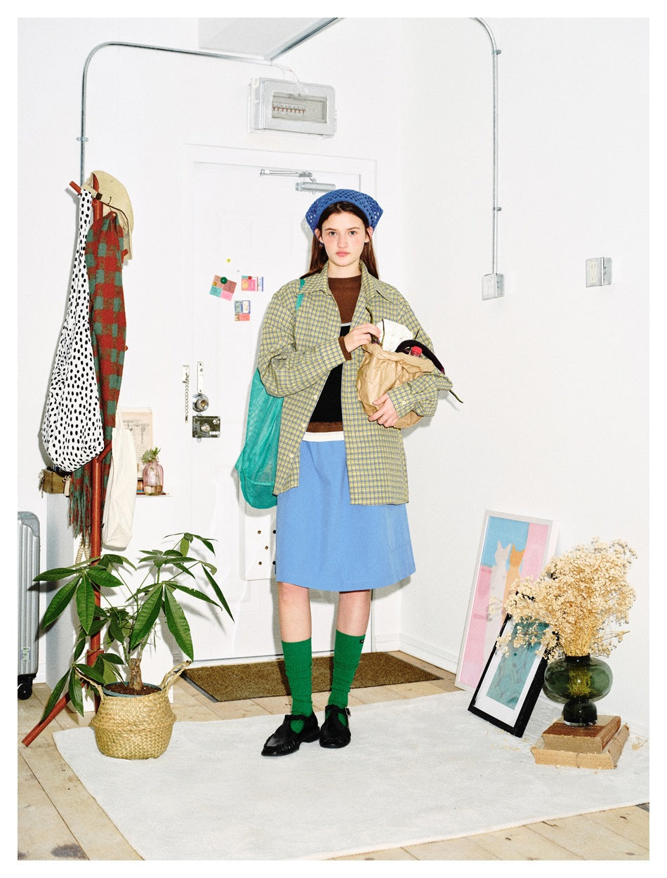 Full-length model wearing a yellow-and-blue plaid button-up shirt, blue skirt, green socks and blue beret.