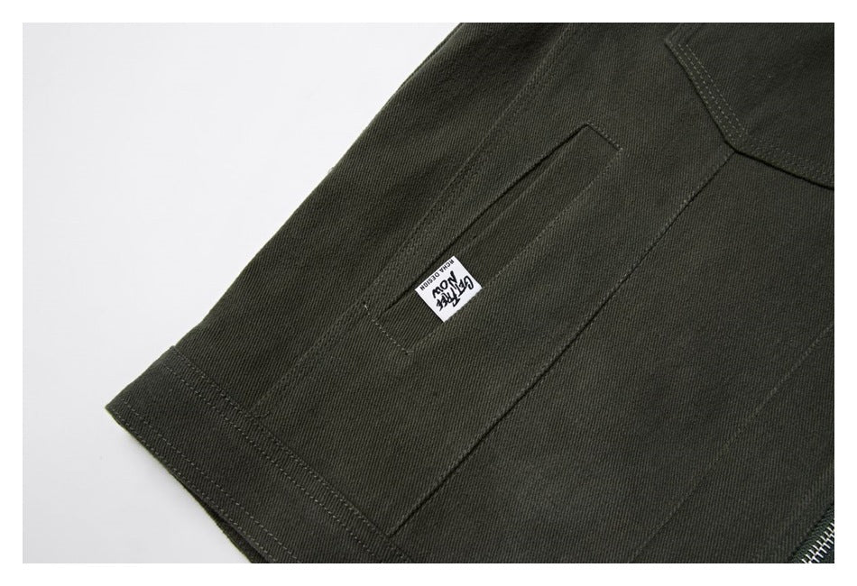 Close-up of a dark olive garment pocket with a small sewn label and a glimpse of zipper teeth.