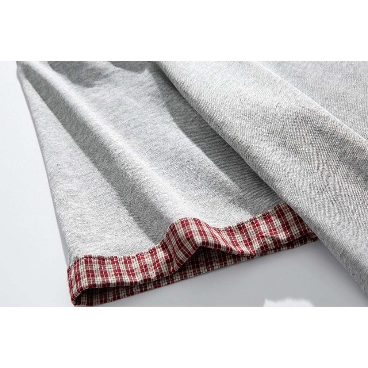 Close-up of a light gray T-shirt hem with red-and-white plaid fabric trim.