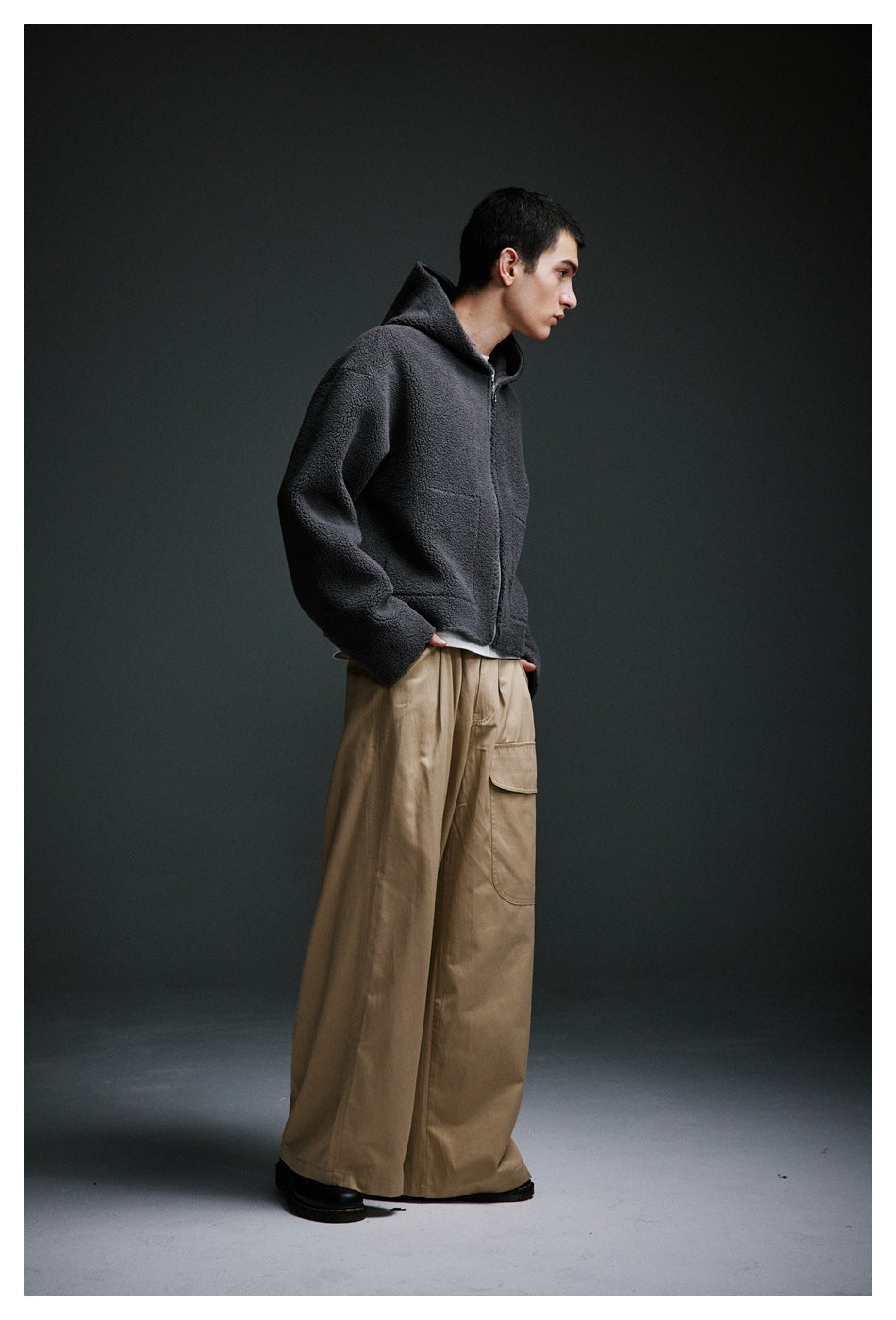 Side view of a model wearing a charcoal hooded jacket and loose taupe cargo trousers.