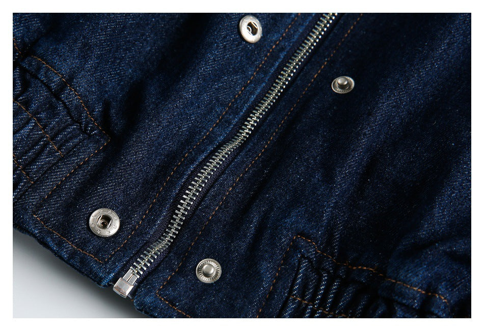 Close-up of a dark indigo denim jacket zipper and silver snaps with orange stitching.