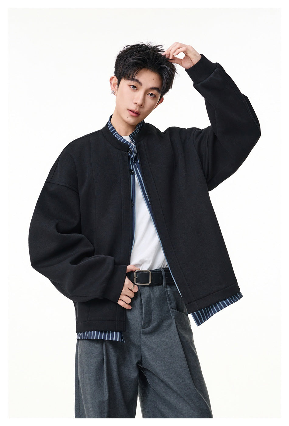 Model wearing an oversized black stand-collar jacket with dark buttons and blue striped shirt trim.