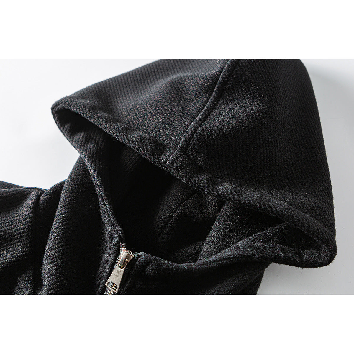 Close-up of a black hood and its seam, with part of a metal zipper pull visible.