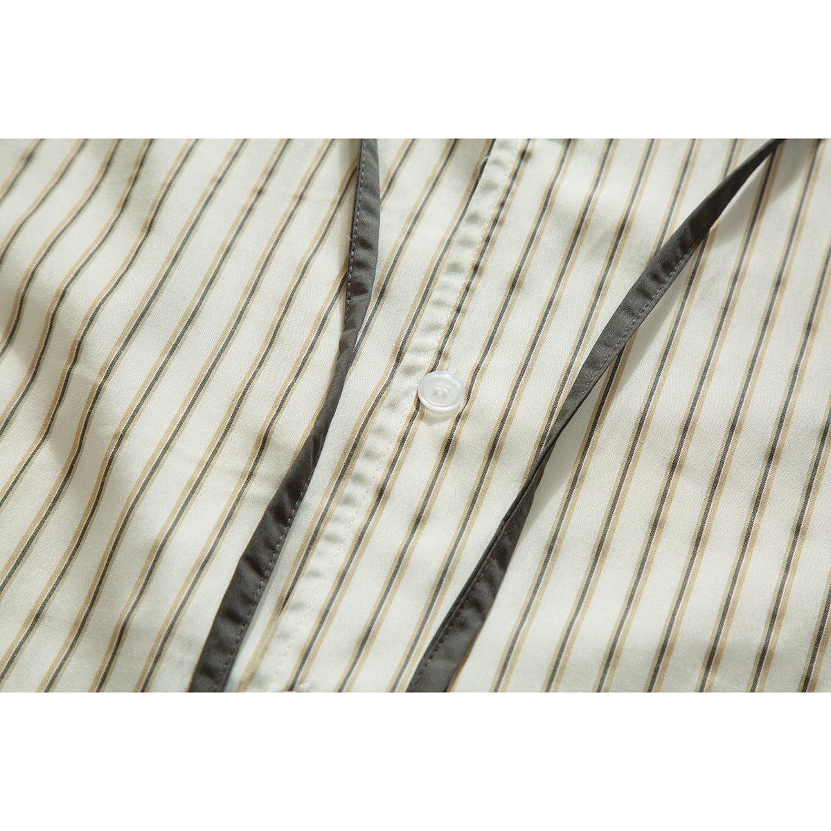 Close-up of a cream striped shirt front with a white button and dark gray trim along the placket.