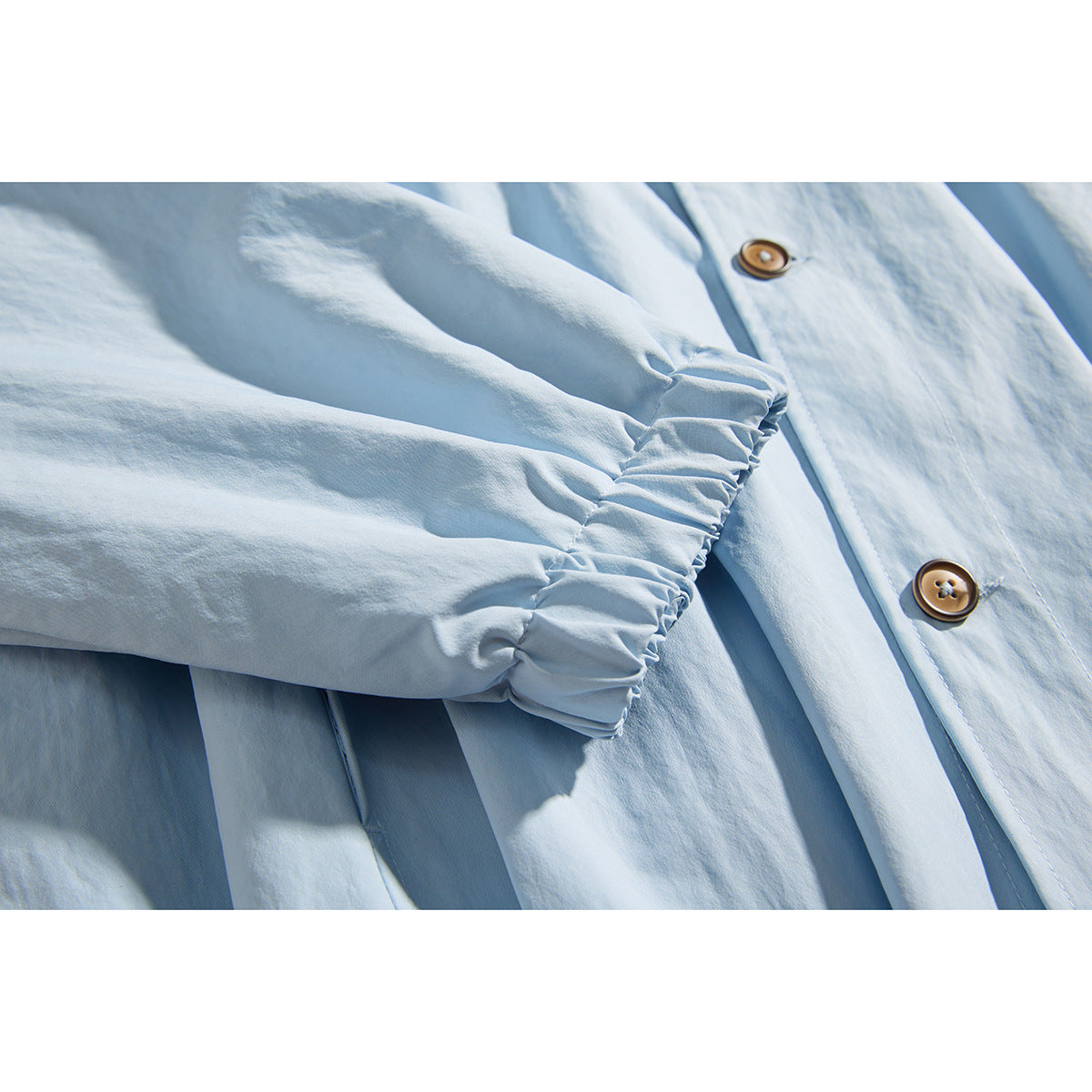 Close-up of a light blue shirt sleeve with an elastic cuff and brown buttons on the placket.