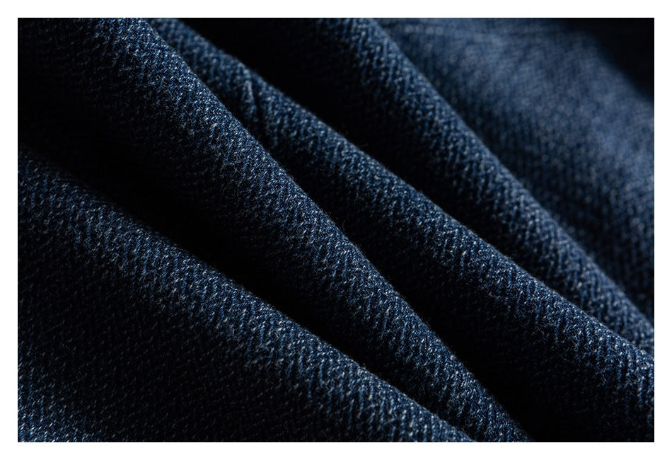 Macro view of dark blue denim fabric folded into soft ridges, showing its woven texture.