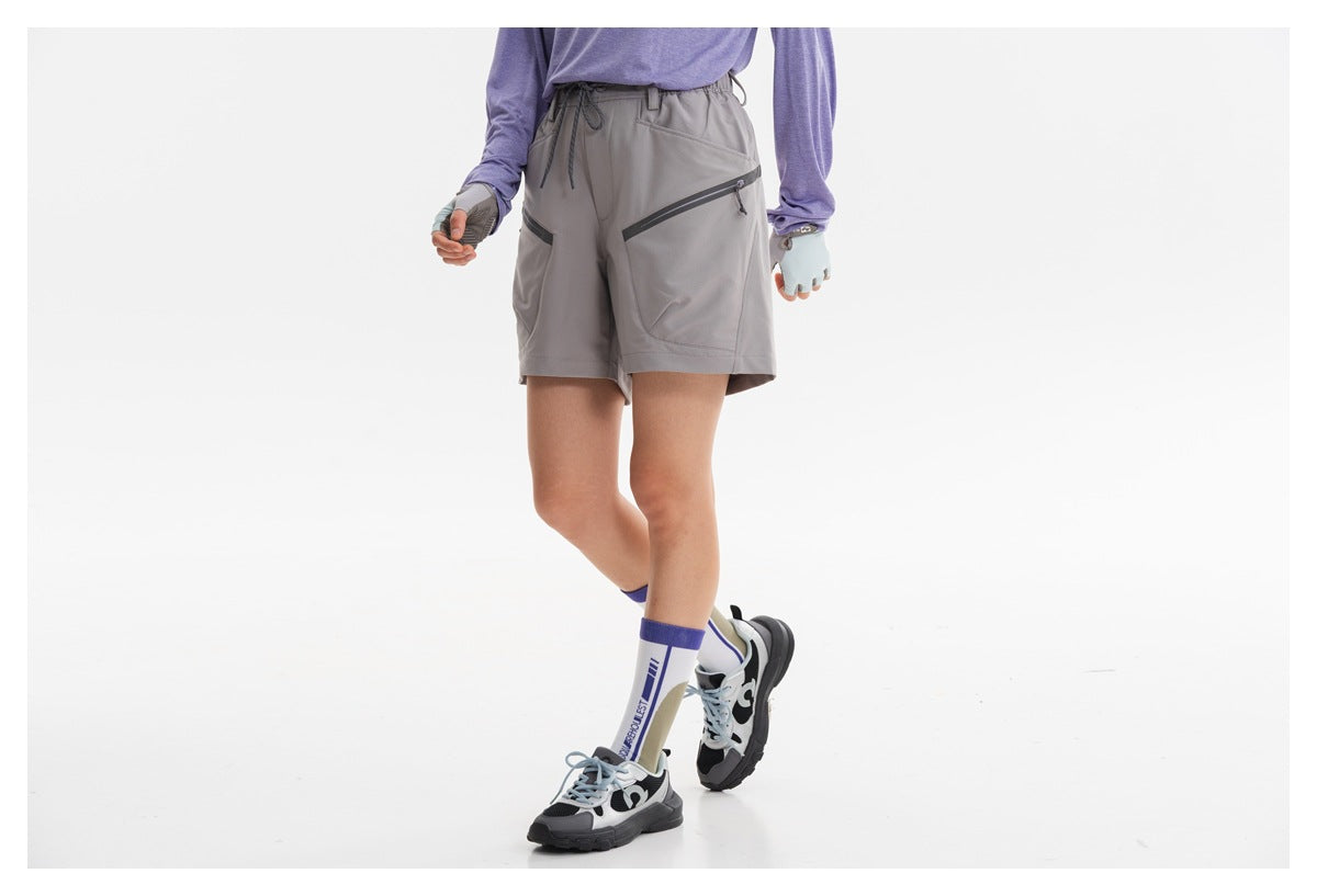 Front view of gray outdoor shorts worn by a model, showing angled zip pockets and a drawstring waist.