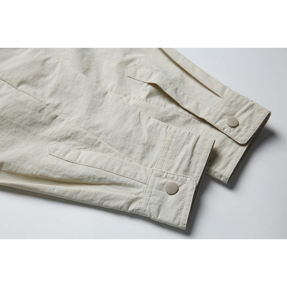 Close-up of the pale beige shirt jacket's sleeve cuff, snap button and stitched panels.