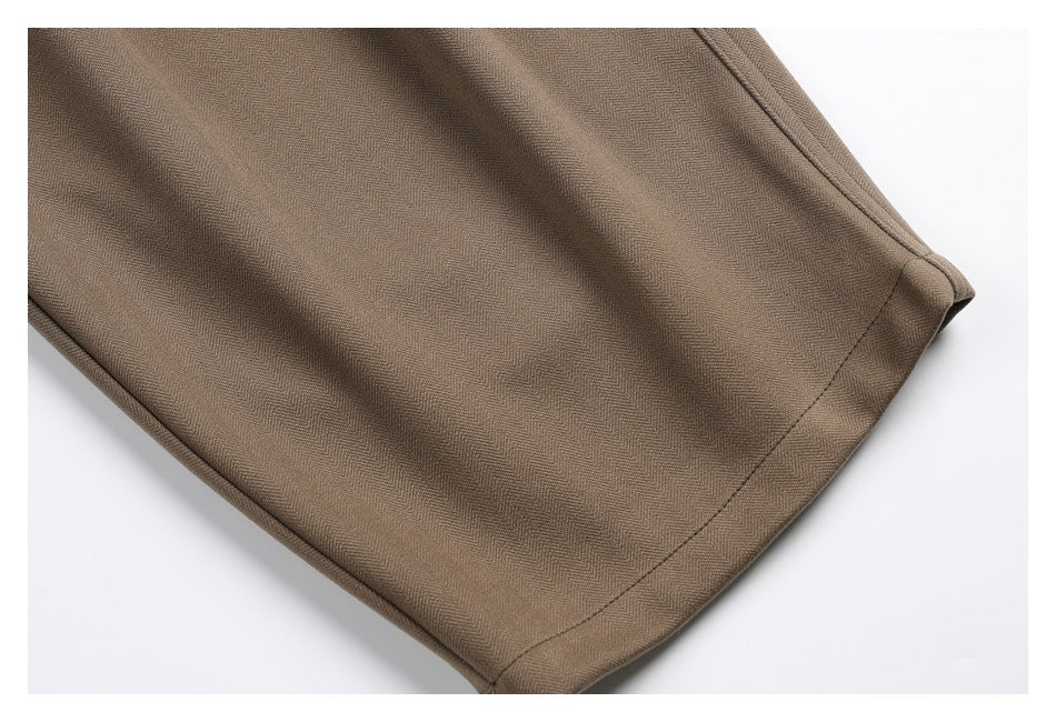 Close-up of a taupe trouser leg showing its stitched hem and subtle woven texture.