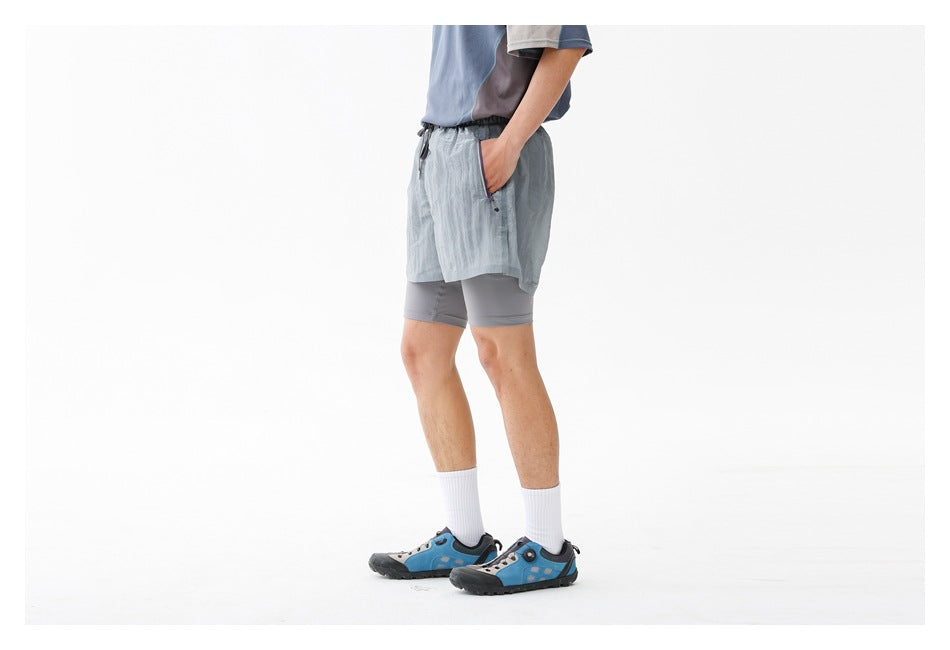Angled view of a person wearing pale blue-gray running shorts with a hand in the zip pocket.