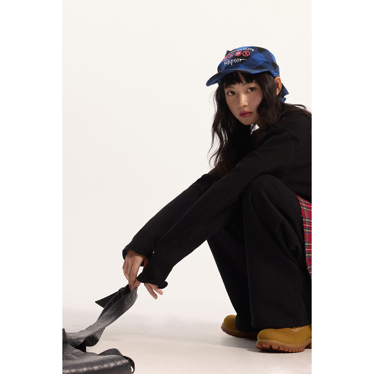 Model wearing a black long-sleeve top with a lace-up neckline, black trousers and a blue patterned cap.