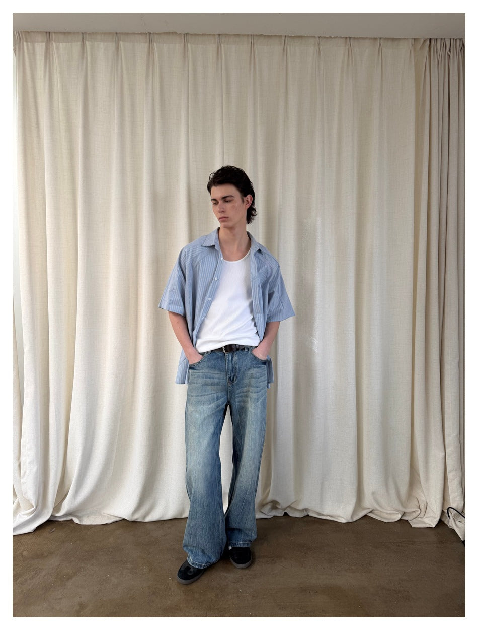 Front view of a model wearing an open blue striped short-sleeve shirt over a white tank top and loose blue jeans.