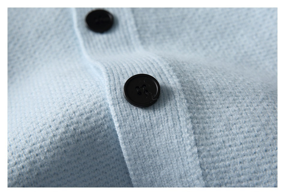 Close-up of two black buttons on the placket of a pale blue knit cardigan.