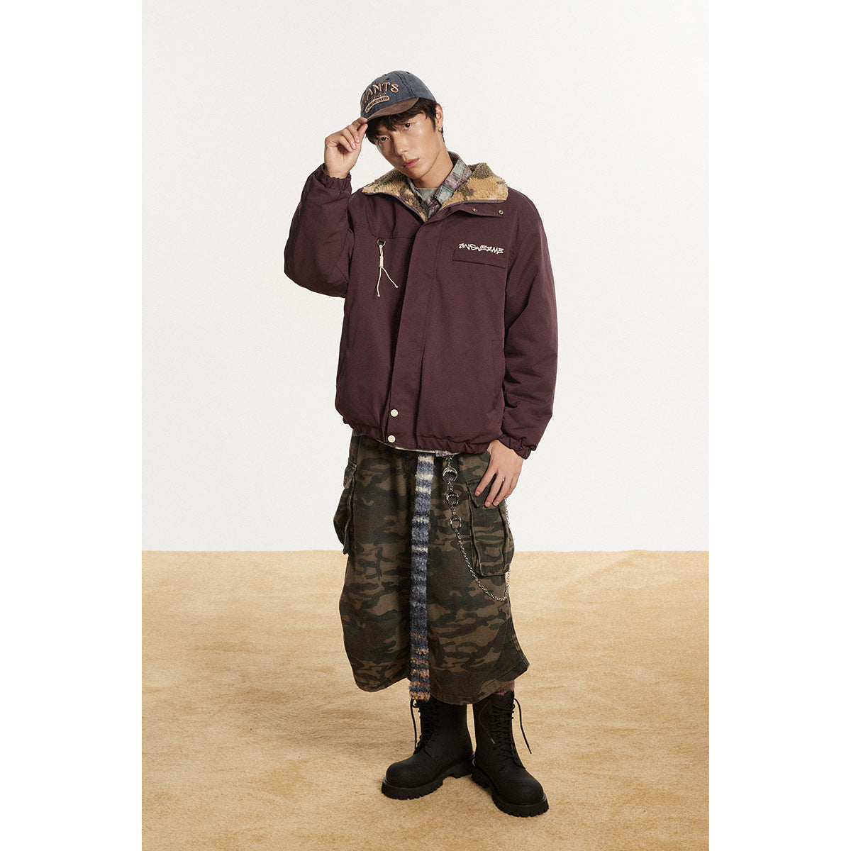 Model wearing a burgundy jacket with a fleece-lined collar, camouflage cargo skirt, cap and black boots.