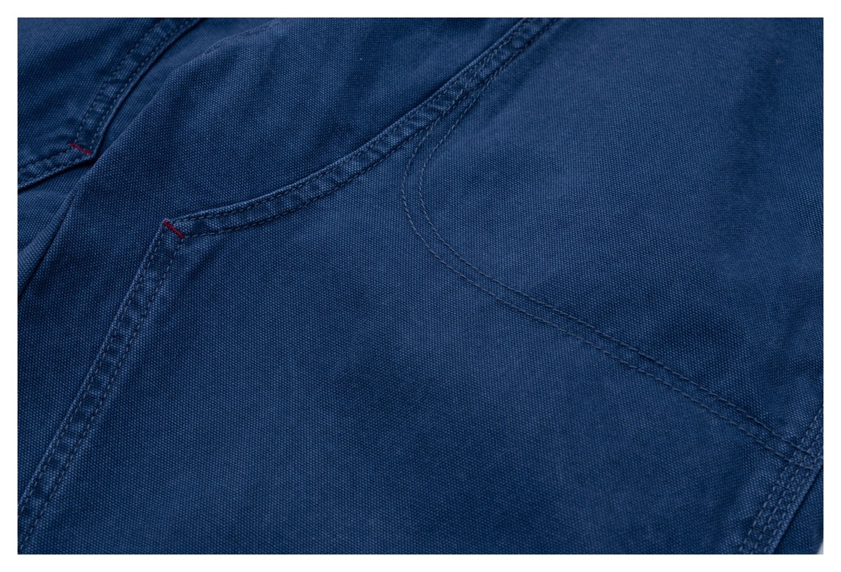 Close-up of dark blue trousers showing curved pocket seams and red bar-tack stitching.