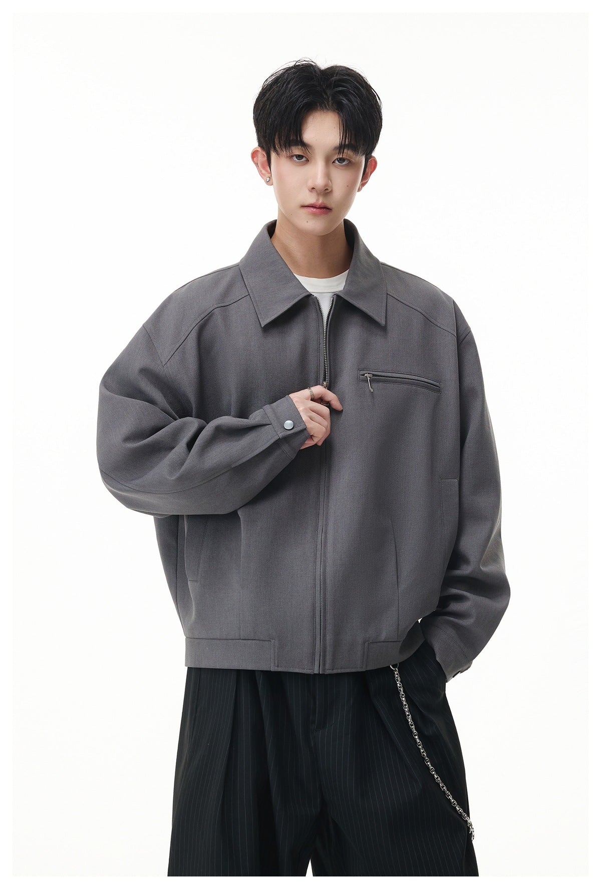 Model wearing a gray zip-front jacket with a pointed collar, chest zipper pocket, and roomy sleeves.
