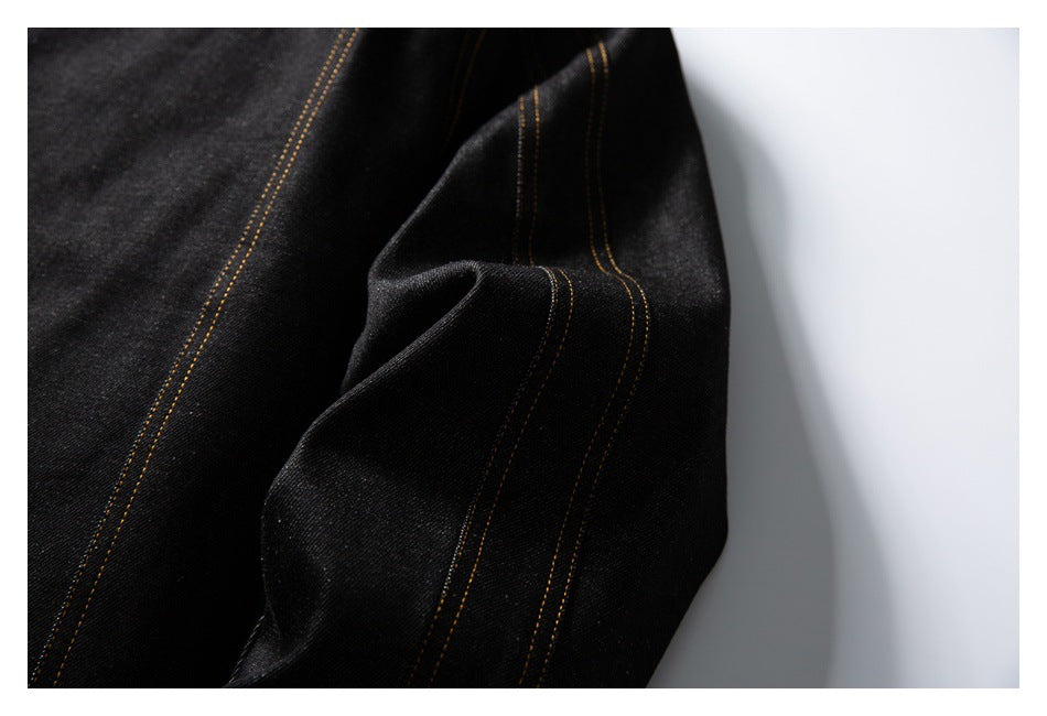 Close-up of black denim fabric and a folded seam with golden contrast stitching.