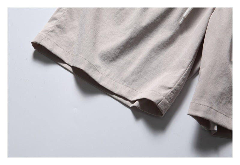 Close-up of the stitched leg hems on light beige shorts.