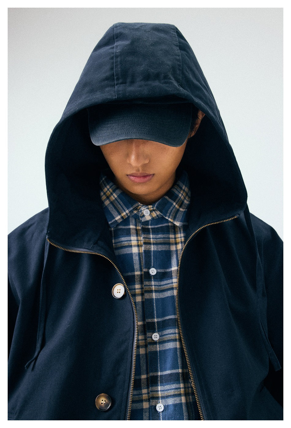 Close-up of the navy jacket's hood, gold-tone zipper and buttons, layered over a blue plaid shirt.