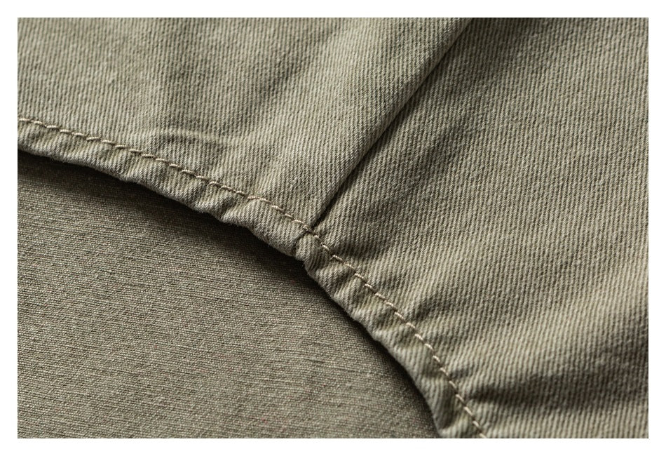 Close-up of a khaki-olive garment edge with a curved stitched hem and visible twill texture.