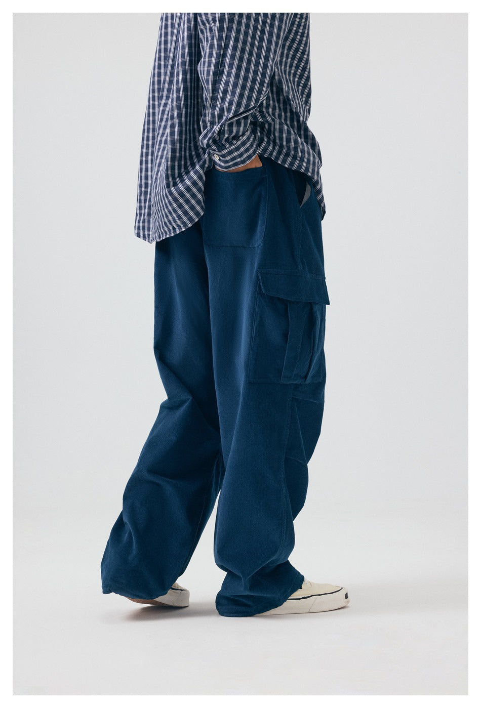 Side view of a model wearing loose navy cargo pants with a blue plaid shirt.