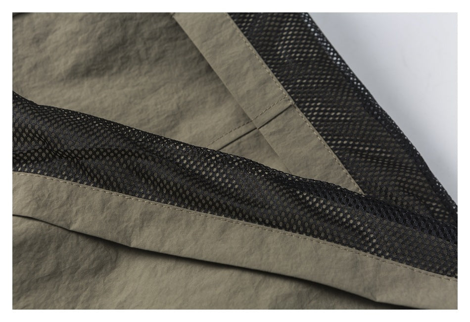 Close-up of khaki shorts showing black mesh lining and stitched fabric panels.