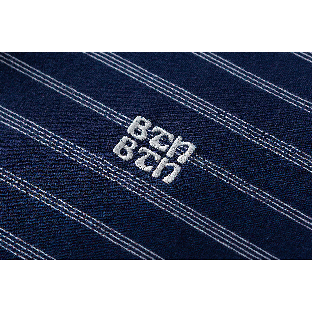 Close-up of white embroidered lettering on navy fabric with thin white stripes.