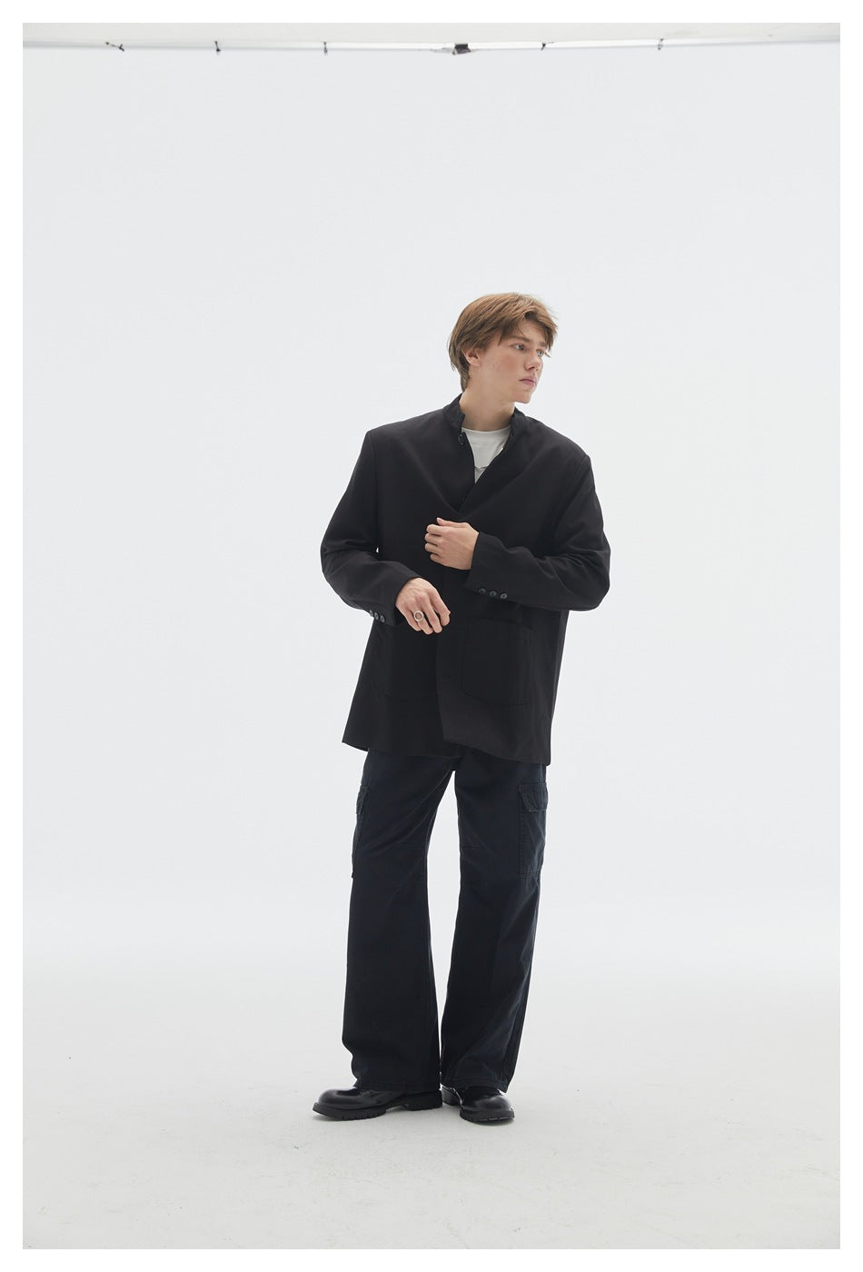 Model wearing a black stand-collar jacket over a white tee with dark cargo pants and black boots, full-length view