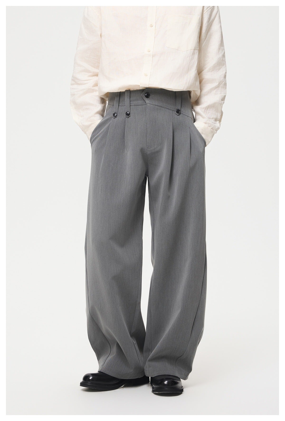 Model wearing gray pleated wide-leg trousers with a cream linen shirt and black leather shoes, front view