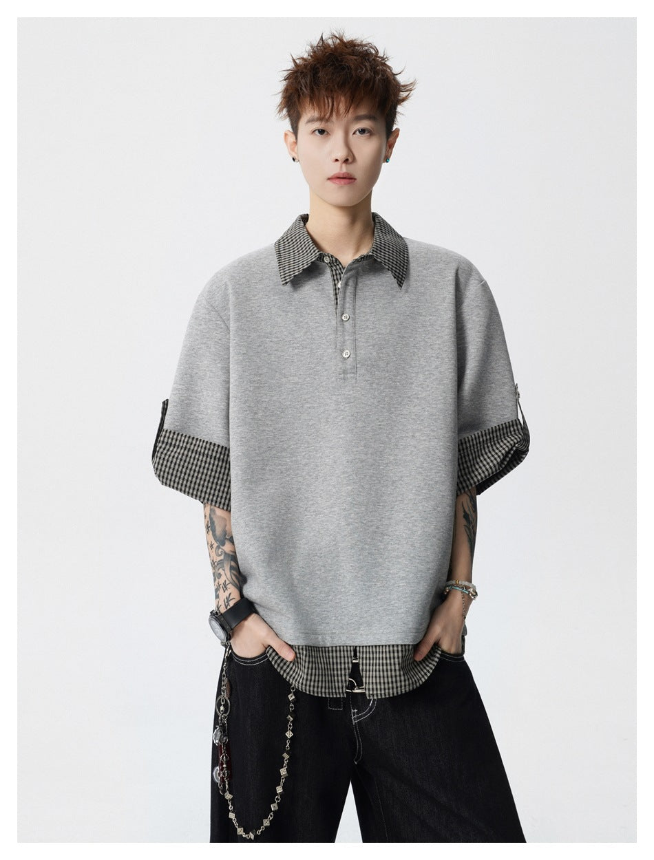 Model wearing an oversized gray polo-style top with a black-and-white checked collar, cuffs, and layered hem.