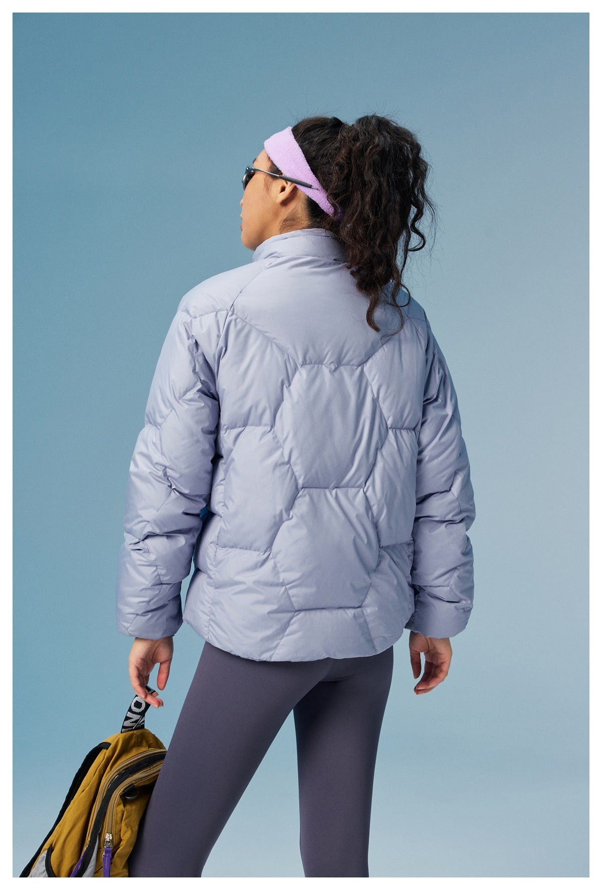 Rear view of a model wearing a lavender-gray quilted jacket with large geometric stitched panels.