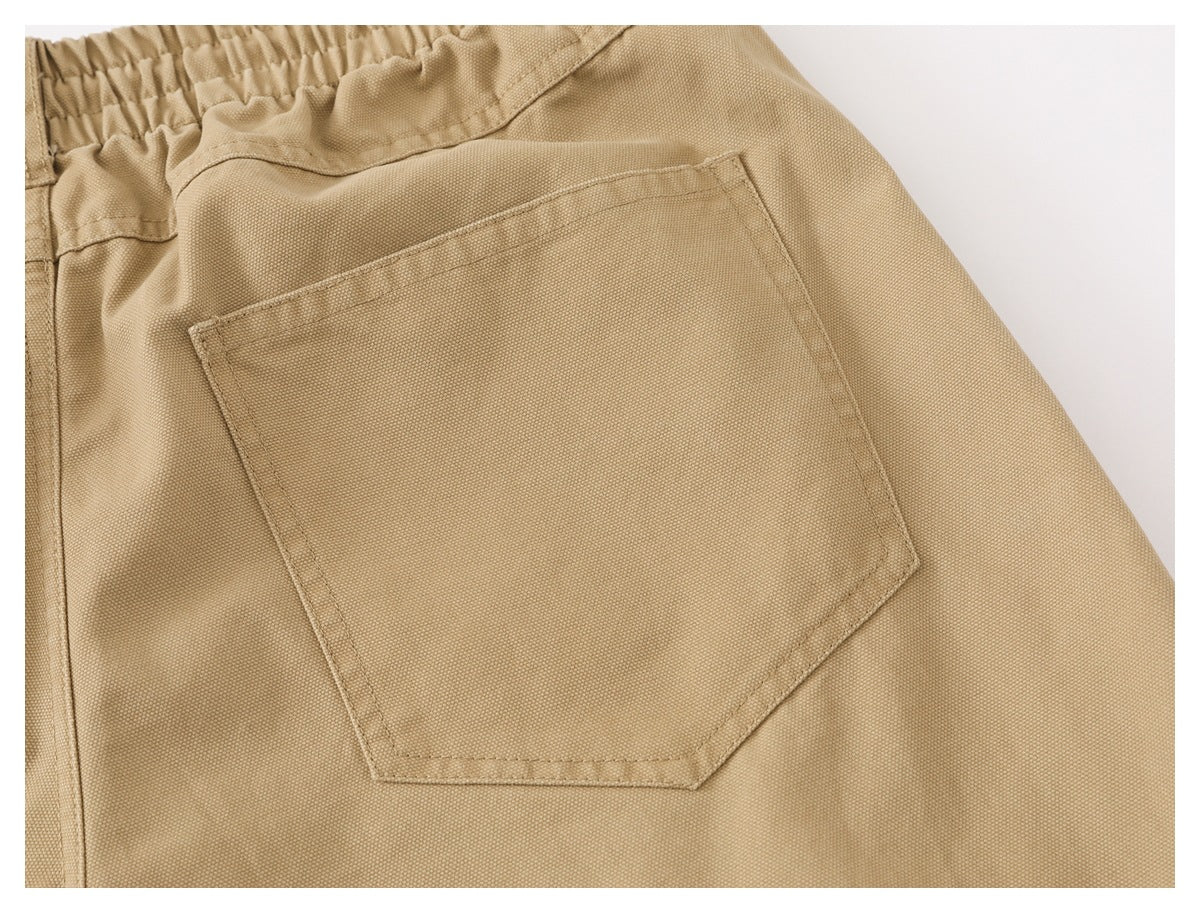 Close-up of a large stitched patch pocket on tan pants, with part of the elastic waistband visible.