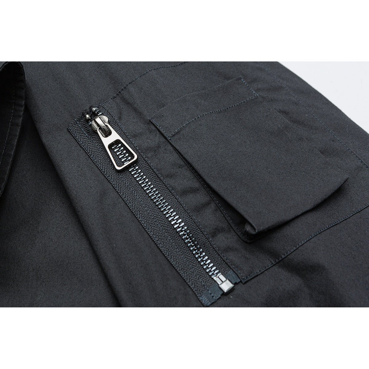 Close-up of a dark jacket's zippered sleeve pocket with a flap and shiny metal zipper.