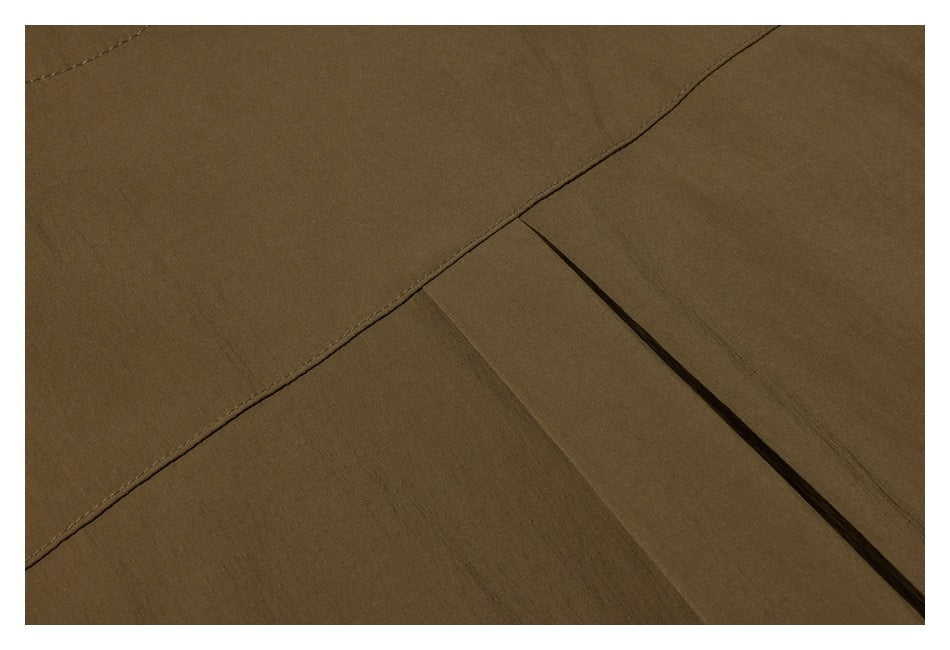 Close-up of a brown garment showing a curved stitched seam and a folded pleat.