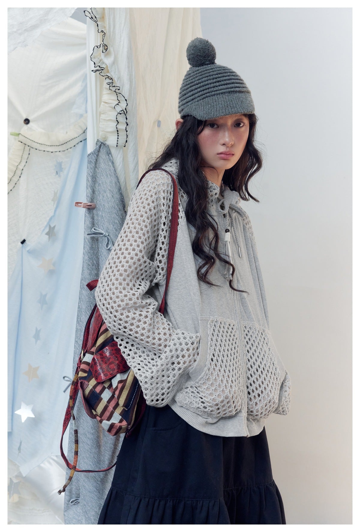 Three-quarter view of a model in a light gray mesh-sleeve zip hoodie and black skirt.