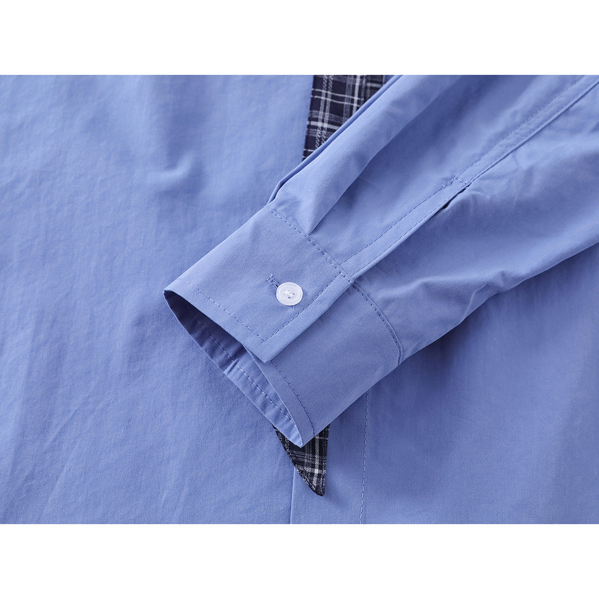 Close-up of a light blue shirt cuff with a white button, with black plaid fabric visible beneath.